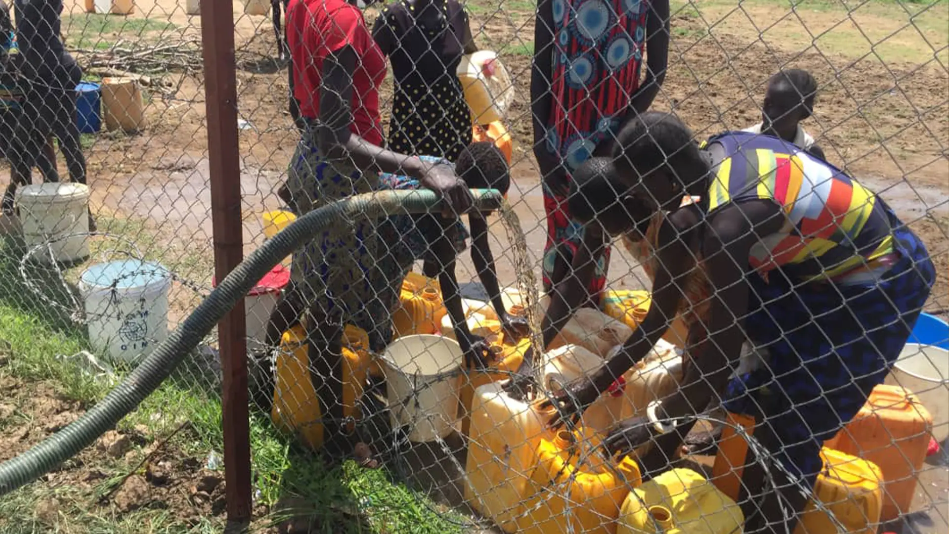 Residents collecting water through a distribution hose at a fenced WASH facility in Lakes State